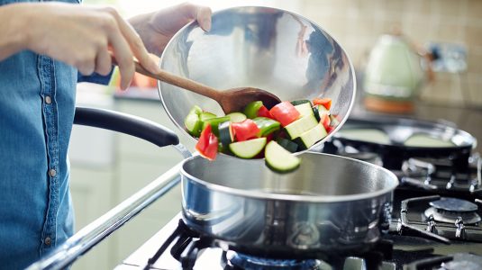 A person adding fresh chopped vegetables in saucepan
