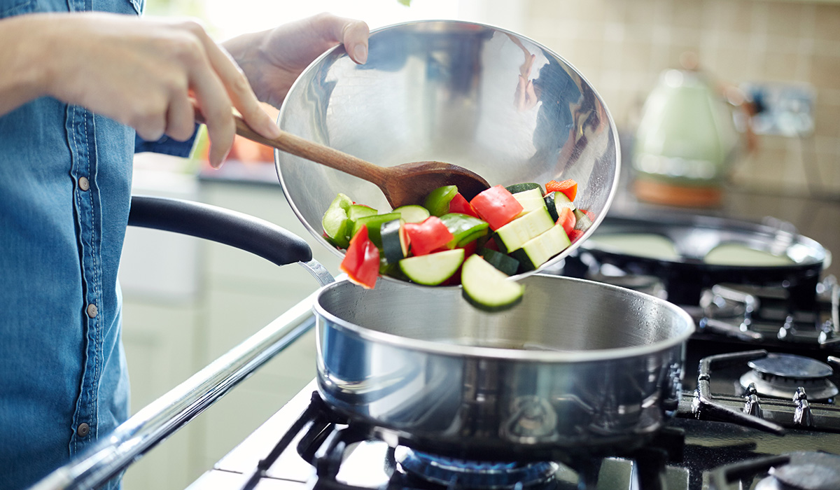 A person adding fresh chopped vegetables in saucepan