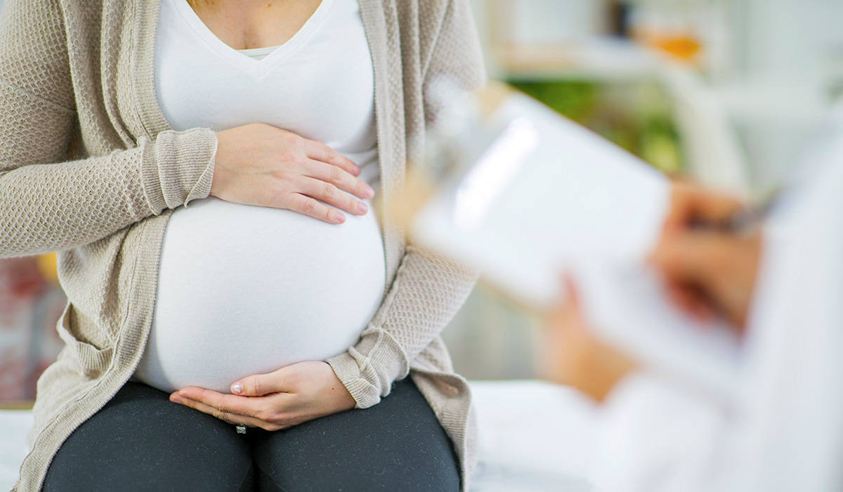 A pregnant woman with her hands on her baby bump while doctor takes notes