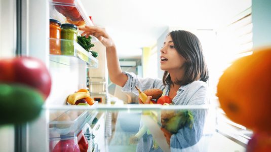 A person picking out fruits and vegetables out of her fridge at home