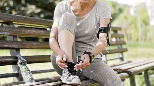 An athletic senior woman tying shoe lace on a sunny day