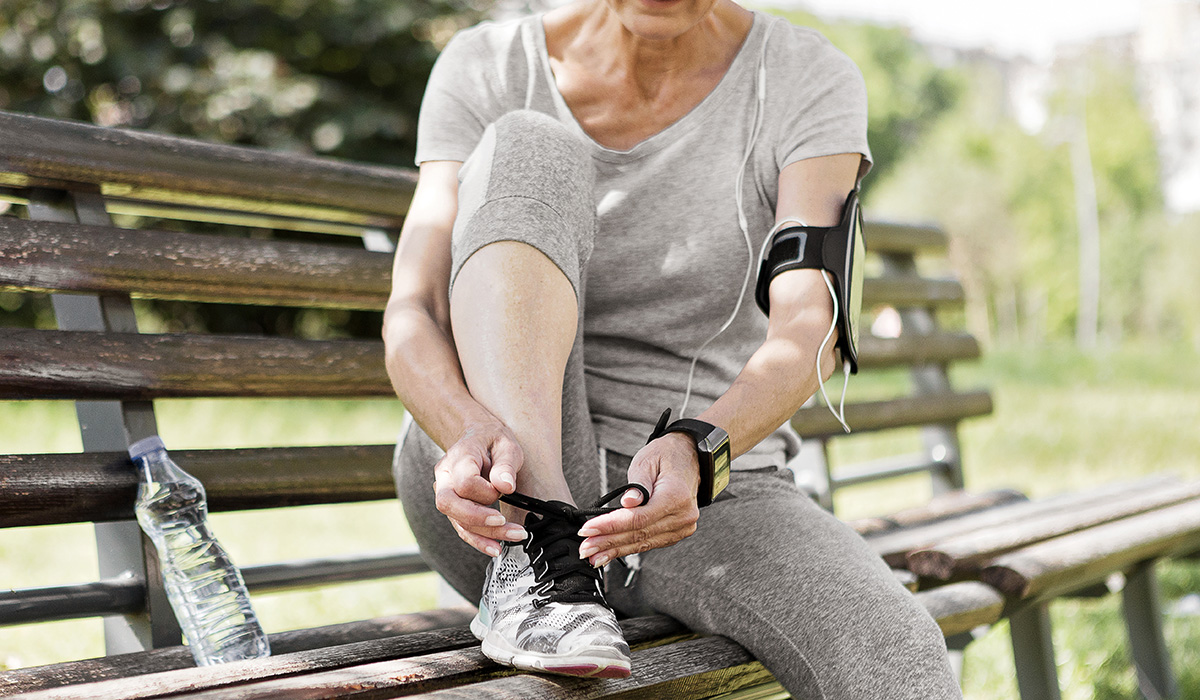 An athletic senior woman tying shoe lace on a sunny day