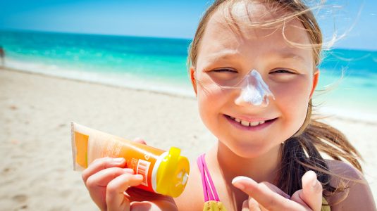 Little girl applying sunscreen on her nose on the beach