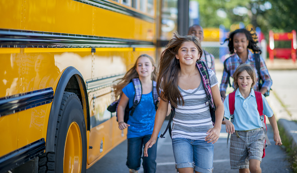 Group of elementary age children running from the bus to class