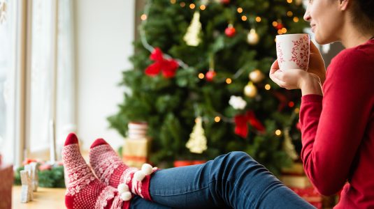 woman drinking hot tea next to a Christmas tree