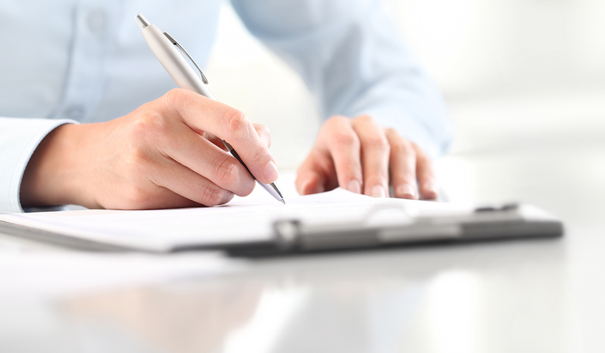 Woman's hands writing on sheet of paper in a clipboard with pen isolated on desk