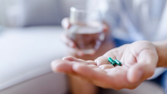 A person taking pills with a glass of water