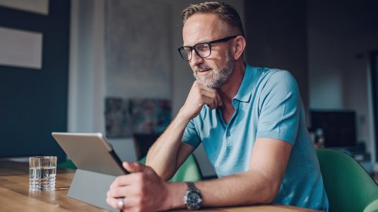 bearded midaged man at a table with digital tablet