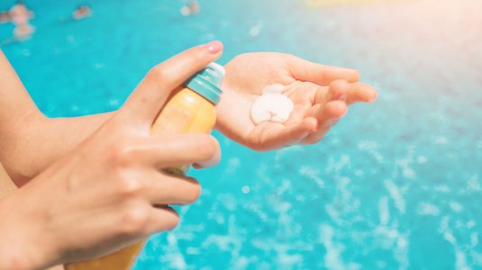 A person applying sunscreen by the pool