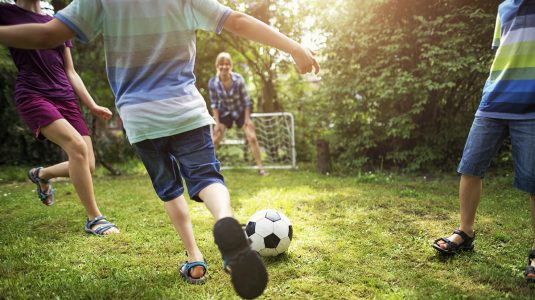 Mother and kids playing soccer in the garden