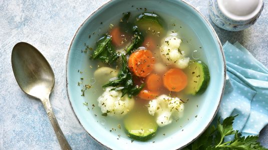 A bowl of vegetable soup with spinach, zucchini, carrot and cauliflower