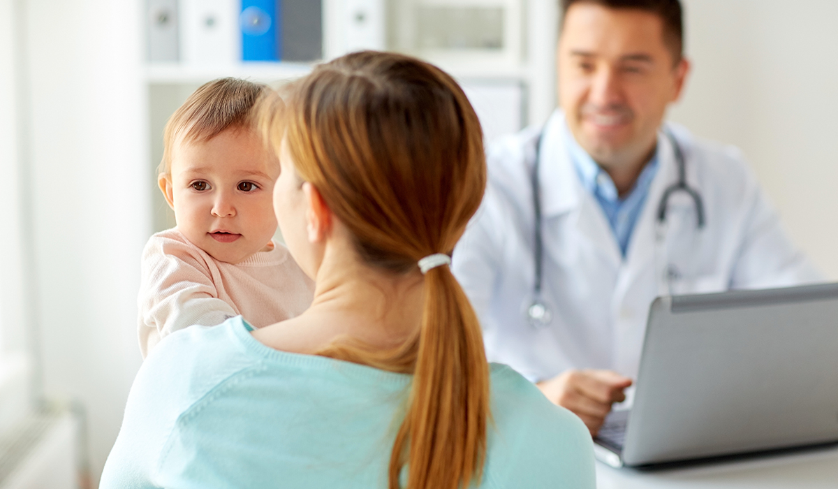 A mom holding a happy baby while speaking to a doctor