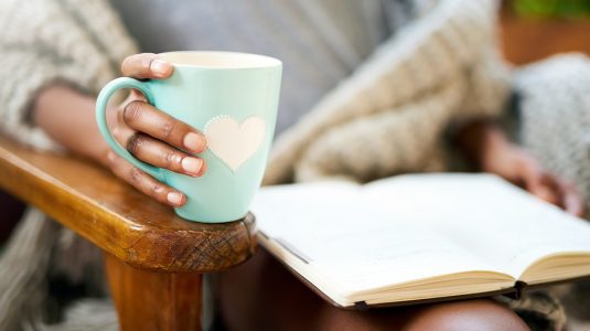 Cropped shot of a woman relaxing with a book and a cup of coffee