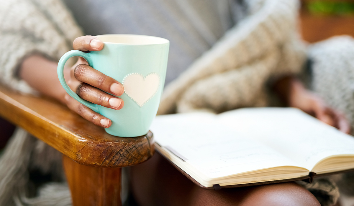 Cropped shot of a woman relaxing with a book and a cup of coffee