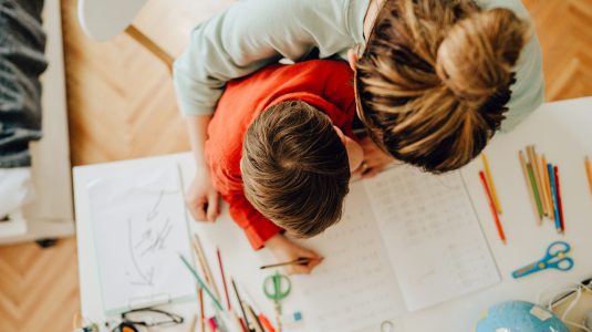 Photo of a young boy being homeschooled by his mother in his bedroom