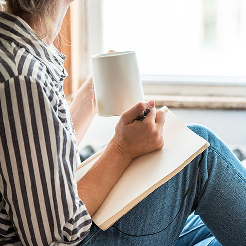 Person writing a journal while drinking coffee