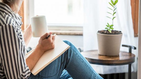 Person writing a journal while drinking coffee
