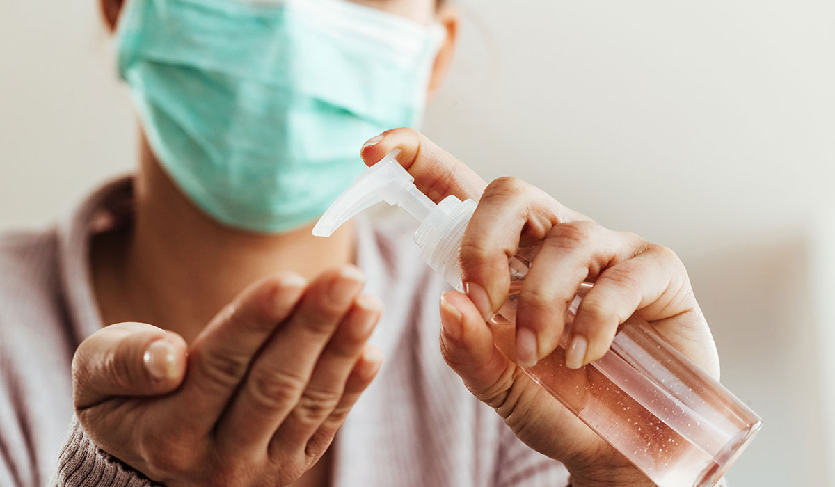 A person wearing a mask using hand sanitizer