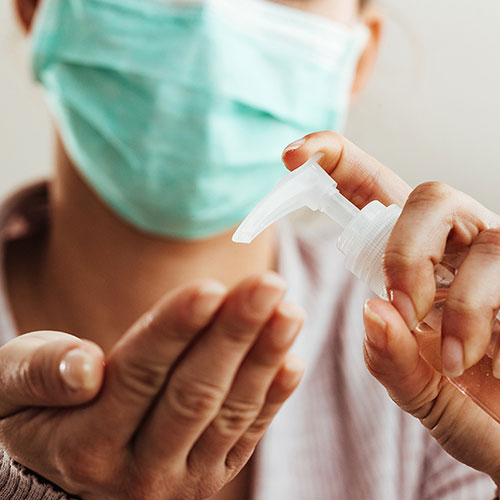 A person wearing a mask using hand sanitizer